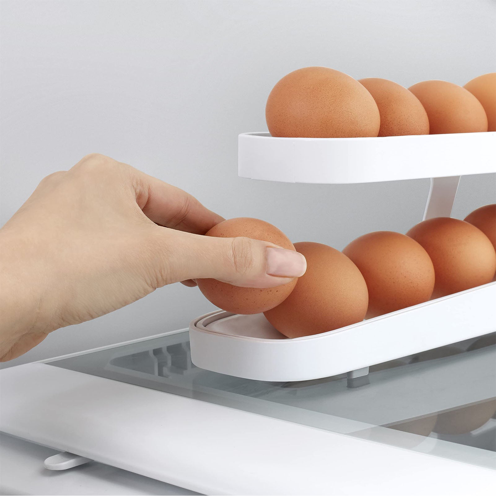Everything Unique's Automatic Rolling Egg Dispenser in a kitchen setting, with someone reaching for an egg from the dispenser.